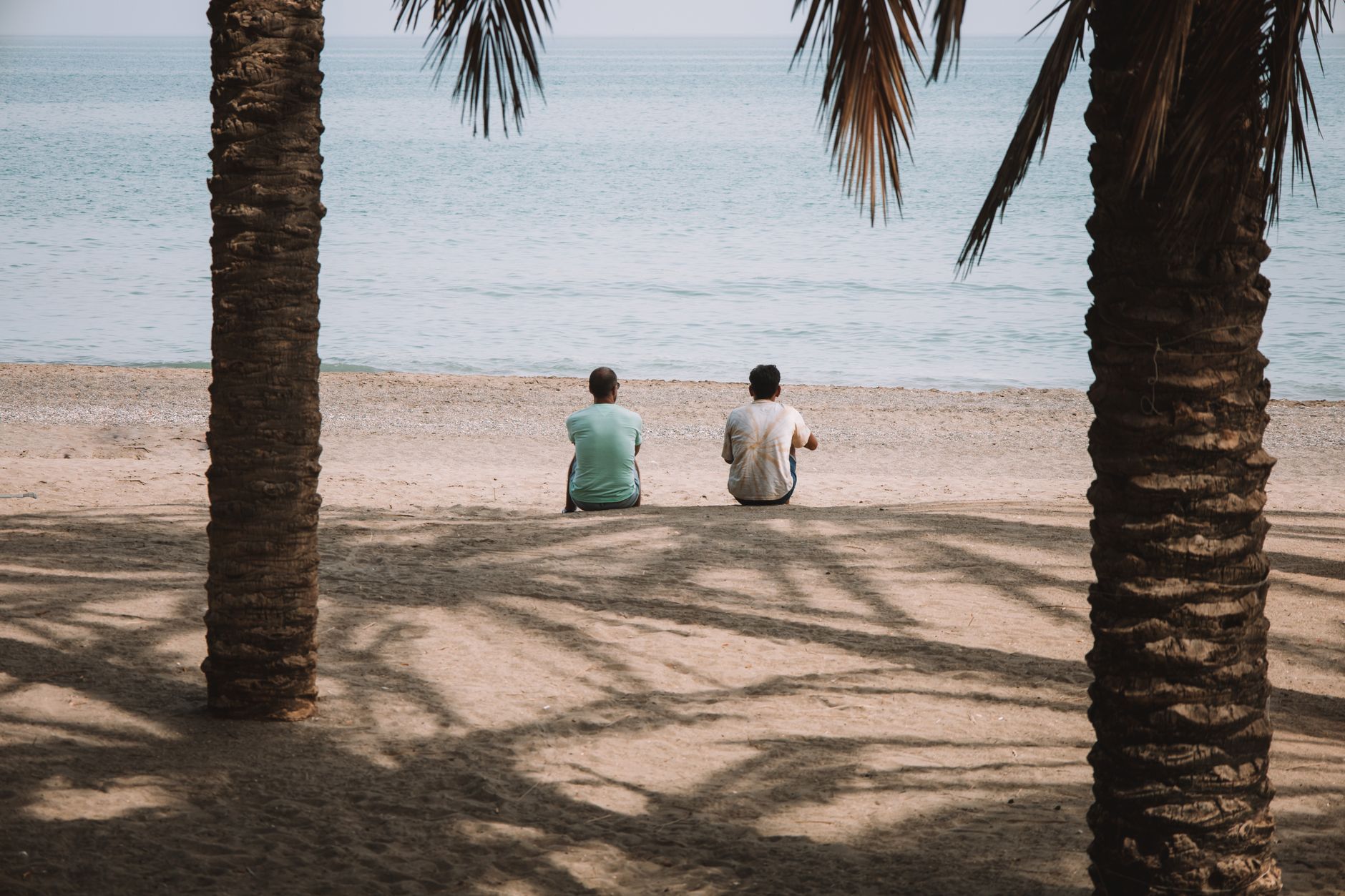 Two people sitting on a Malaga beach framed by palm trees