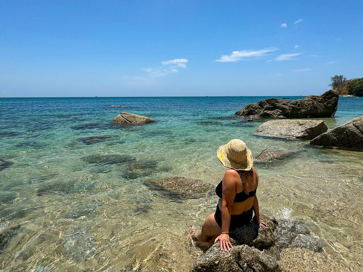 Mairin in a sun hat sitting by clear turquoise water on a tropical beach