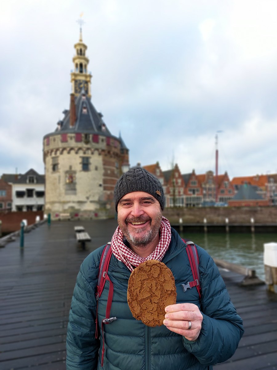 Todd holding a large spiced biscuit by a harbour tower in Hoorn, Netherlands