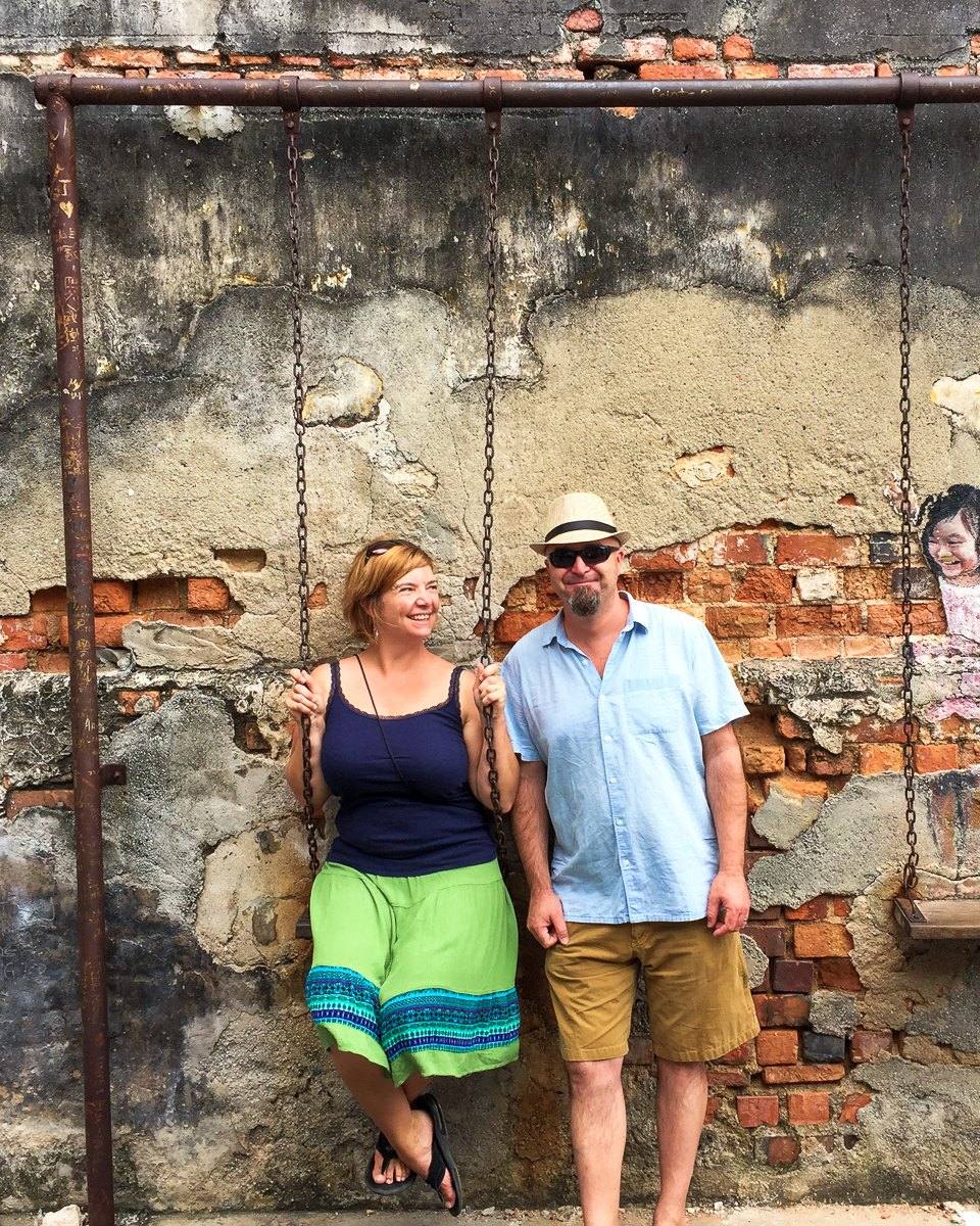 Mairin and Todd dwarfed by a giant buttress-rooted rainforest tree in the tropics