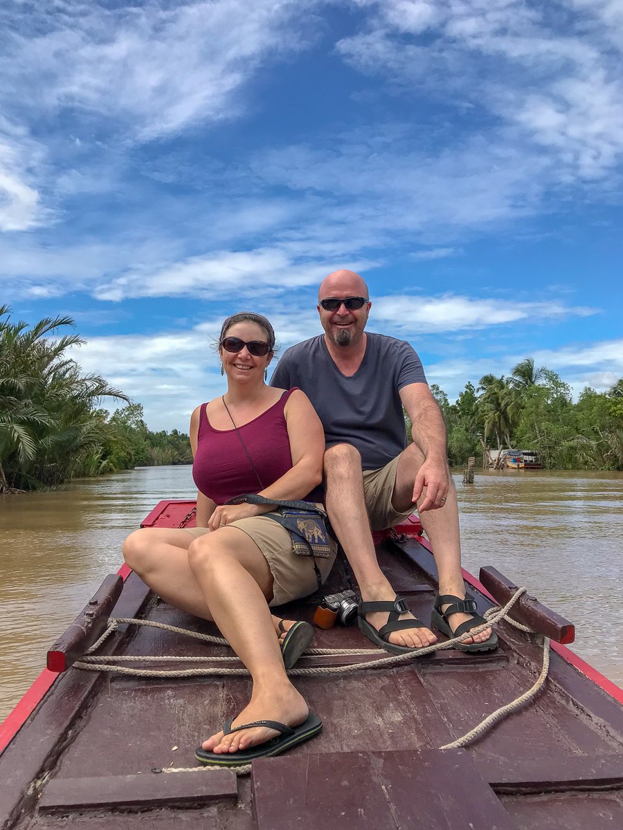 Mairin and Todd on the prow of a wooden boat on a palm-lined river in the Mekong Delta, Vietnam