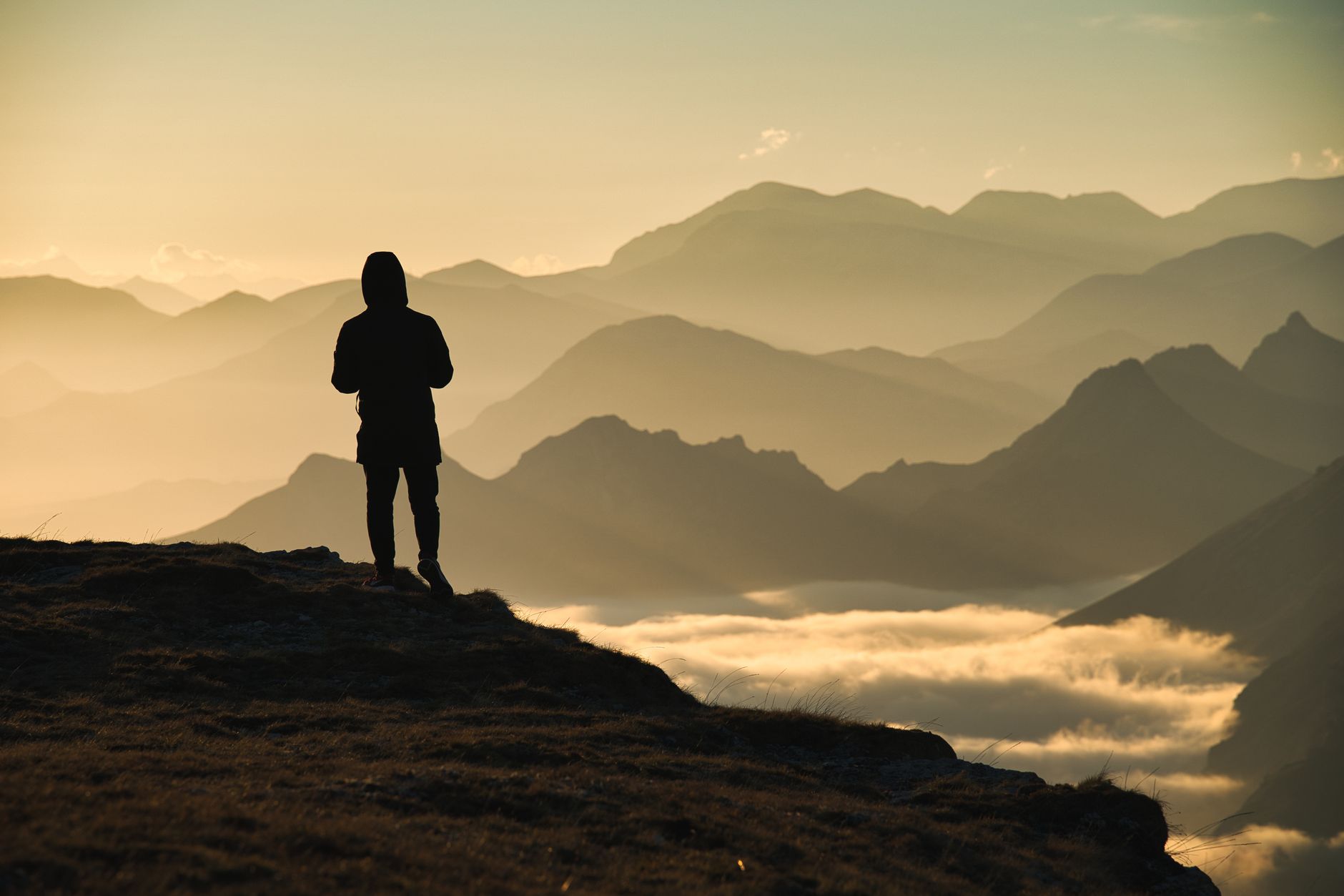 A lone figure standing on a ridge looking out at mountains