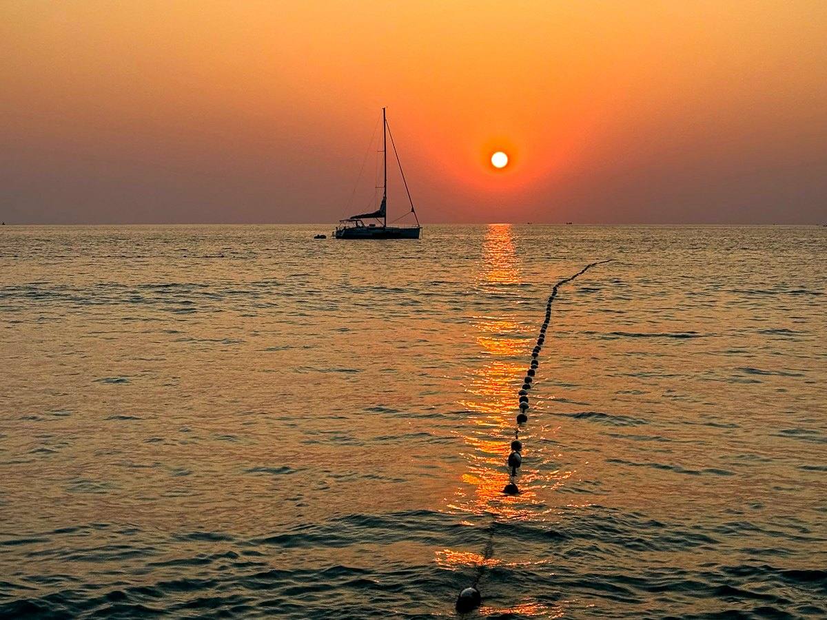 A lone sailboat silhouetted on a calm sea under a deep orange sunset