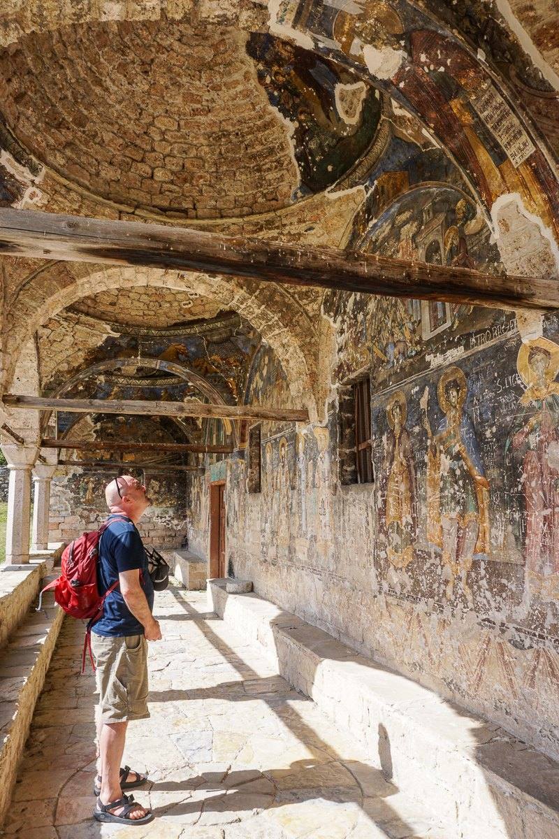 Todd looking up at faded Byzantine frescoes in the portico of an old stone monastery